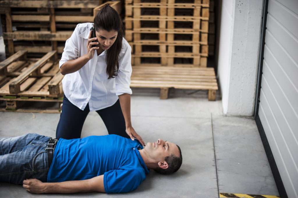 Man im blauen Shirt liegt am Boden und eine Frau ruft den Rettungsdienst