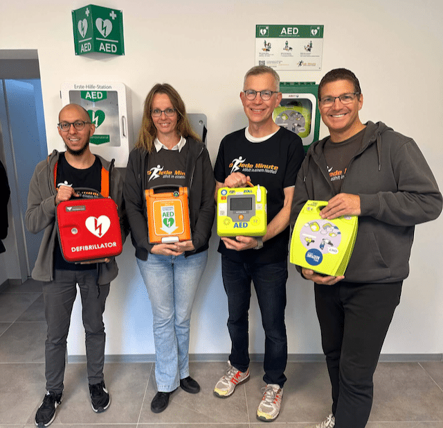 Vier Mitarbeiten vom Jede Minute Team mit jeweils einem Defibrillator in der Hand